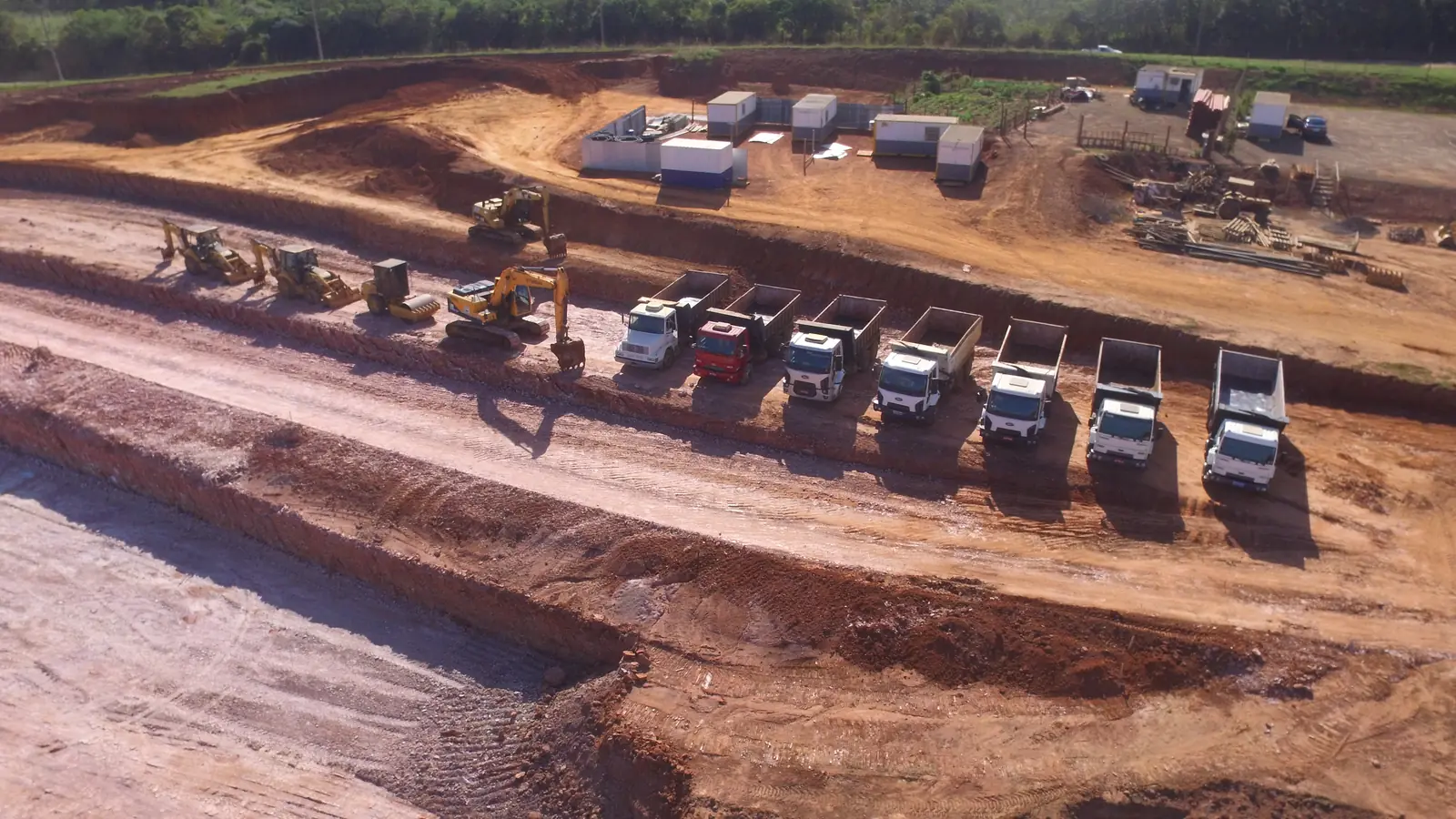 Vista aérea de caminhões e máquinas alinhados em obra de terraplenagem