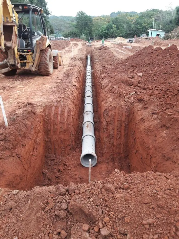 Tubulação instalada em vala aberta, com retroescavadeira ao fundo